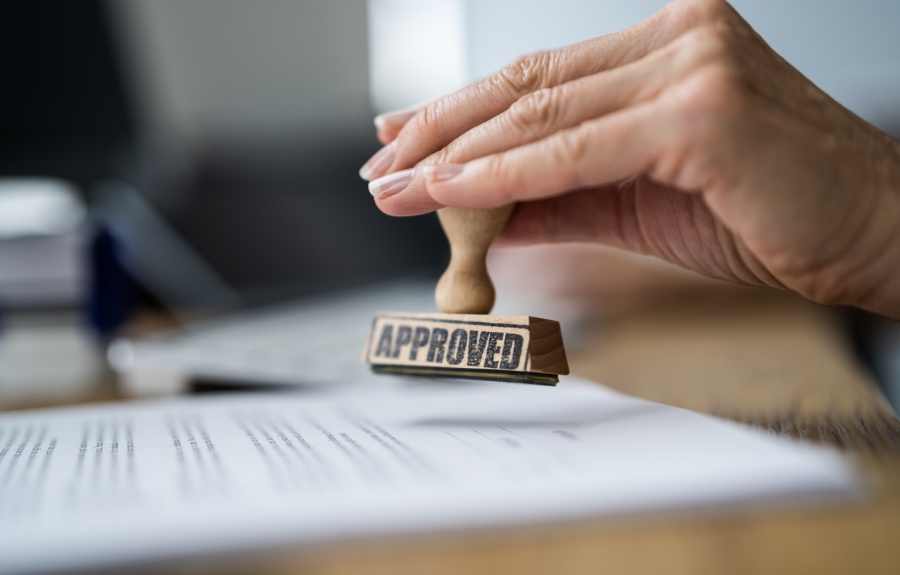 A hand holds an approved stamp over permit application documents on a desk.